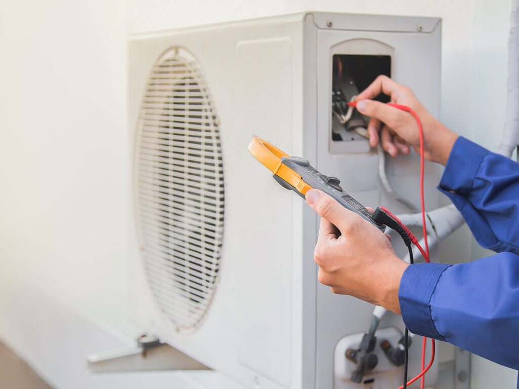 Technician testing an outdoor AC unit with an electrical meter.