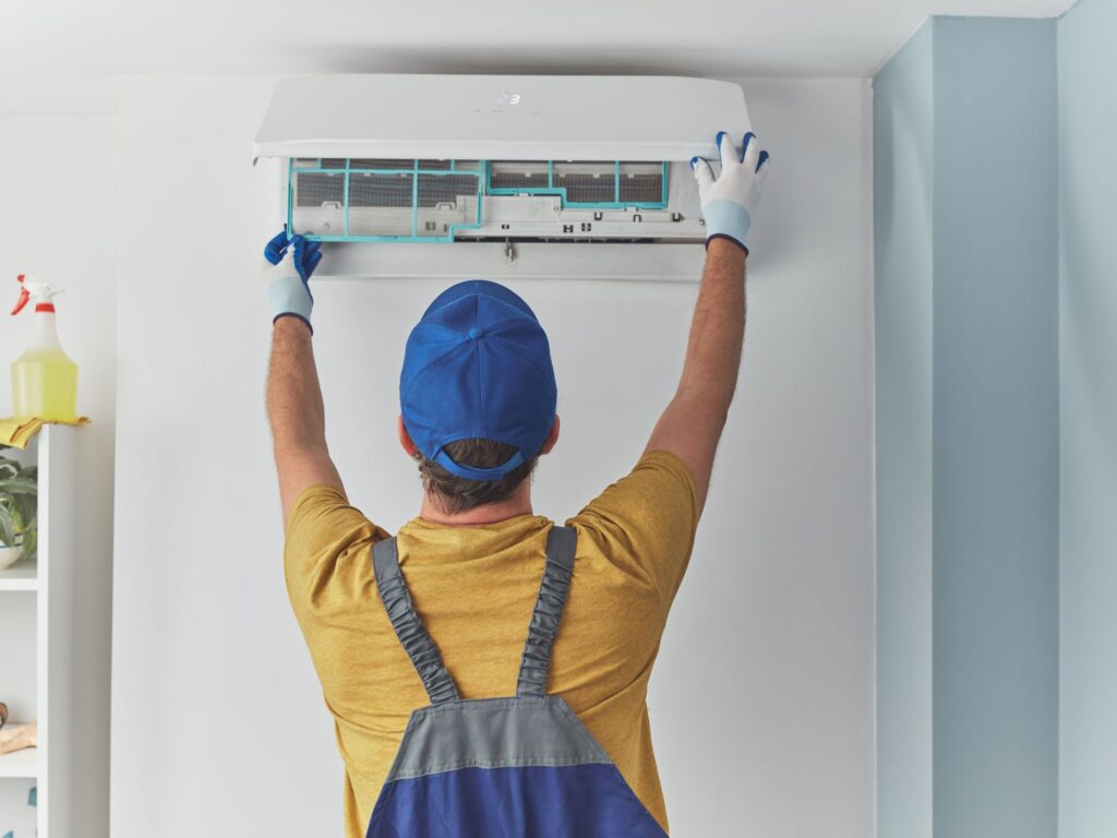 HVAC worker opening and cleaning the filter cover on an indoor AC.