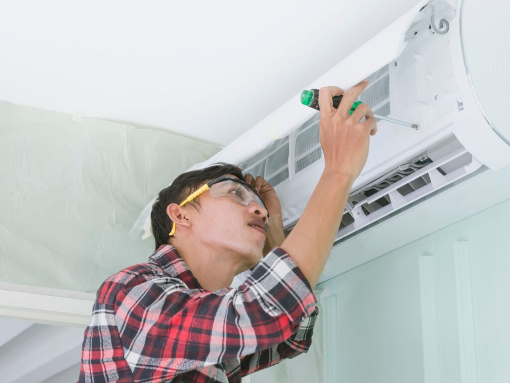 Technician repairing an indoor AC unit with a screwdriver.
