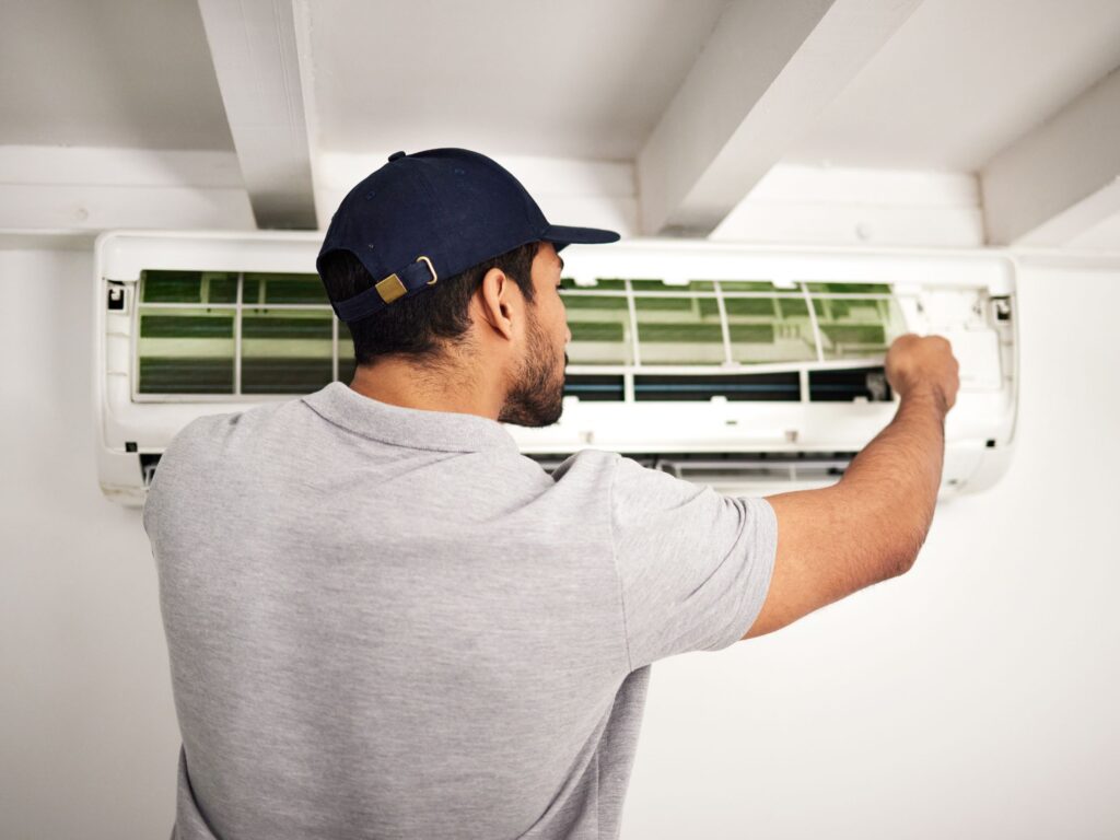 Technician servicing the front panel of a wall-mounted air conditioner.