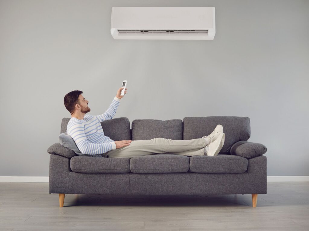 Man relaxing on a couch while controlling the AC with a remote.