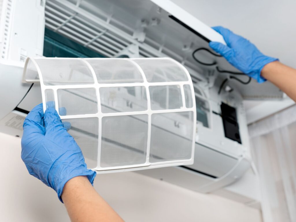 Gloved hands removing a washable filter from an indoor AC unit.
